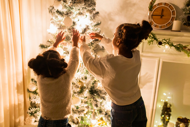 Deux enfants décorent un sapin de Noël avec des guirlandes lumineuses